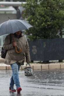 Pessoa a caminhar abrigada com guarda-chuva aberto durante chuva